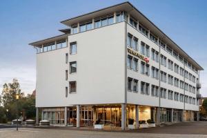 un grand bâtiment blanc avec une façade de magasin dans l'établissement Vienna House Easy by Wyndham Günzburg, à Guntzbourg