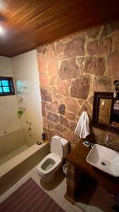 La salle de bains est pourvue d'un mur en pierre, de toilettes et d'un lavabo. dans l'établissement Pousada Casa Fraternità, viva momentos de tranquilidade em contato com a natureza., à Andaraí