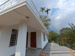 a white house with a walkway and a palm tree at 3R Residency Munnar in Munnar