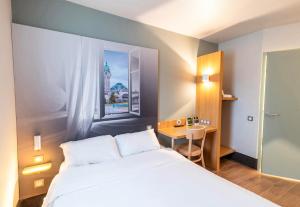 1 dormitorio con cama blanca, escritorio y ventana en B&B HOTEL Limoges 1, en Limoges
