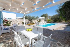 un patio con una mesa y sillas blancas y una piscina en Kalathos Dream Villas, en Kalathos