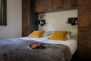 a bed with yellow pillows and a book on it at Lodge Eik Nunspeet Veluwe in Nunspeet