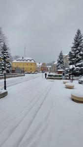 a snow covered street with a yellow building in the background at Apartament u Danusi in Złoty Stok