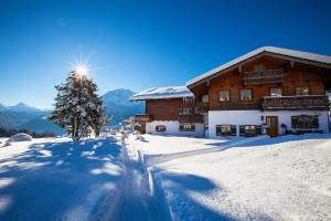 un edificio cubierto de nieve con un árbol delante de él en Alpenpension Ettlerlehen en Ramsau