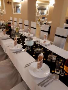 a long table with white plates and silverware at Hotel Baltazar Pułtusk in Pultusk