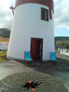 ein Leuchtturm mit zwei blauen Stühlen davor in der Unterkunft Moinho Mó da Praia in Praia da Graciosa