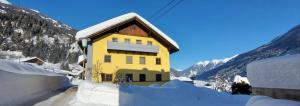 une maison jaune dans la neige avec des montagnes dans l'établissement Appartement Kerschbaumer, à Rangersdorf