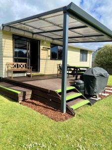 a covered deck with a picnic table and a grill at Relax Cabin - Waihi Beach Holiday Home in Waihi Beach