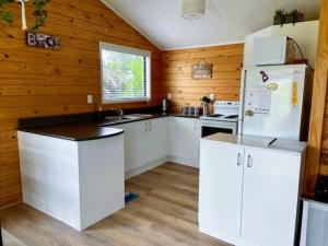 a kitchen with white cabinets and a white refrigerator at Relax Cabin - Waihi Beach Holiday Home in Waihi Beach