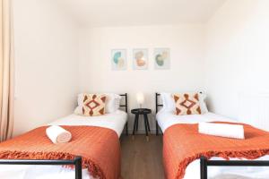 two beds in a room with white walls and orange sheets at Amaryllis- 2 Bedroom Flat in Southampton