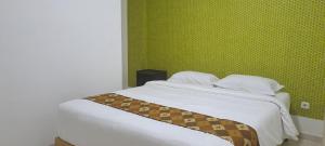 a bedroom with a white bed with a green wall at ARIMBI GUEST HOUSE in Batu