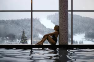 a woman sitting next to a window next to a swimming pool at Hotel Podgorie Spa in Bukovel +145 photos