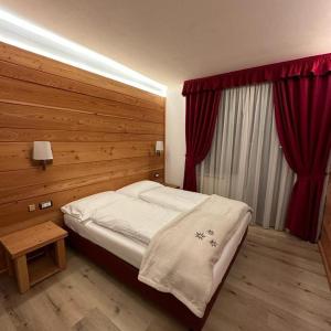 Albergo Garni Martina في كاريسولو: غرفة نوم بسرير ونافذة ذات ستائر حمراء