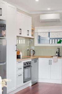 a kitchen with white cabinets and stainless steel appliances at The Elements l Fire l 4 Stunning Apartments each with Private Outdoor Dining l Walk to the Beach l Family Friendly l Wifi l Netflix l Outdoor Shower l Communal BBQ Pavilion and Lawn Area l in Christies Beach
