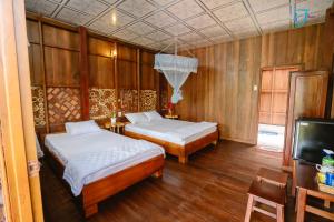 Muong Dinh Lodge في Ấp Nhơn Bình: سريرين في غرفة بجدران خشبية وتلفزيون