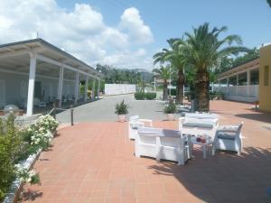 un patio con sillas blancas, mesas y palmeras en Villaggio La Feluca, en Isca sullo Ionio