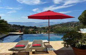 um guarda-sol vermelho e duas cadeiras ao lado de uma piscina em Villa Thalassa Art' B&B em Le Lavandou