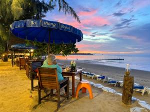 a woman sitting at a table under an umbrella on the beach at Ao Thong beach Resort in Khao Lak