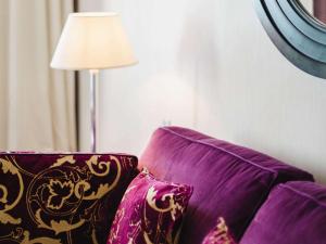 a purple couch with pillows next to a lamp at Le Grand Hotel de Cabourg - MGallery Collection in Cabourg