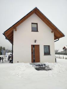 Biały dom z drewnianymi drzwiami w śniegu w obiekcie Domek pod Żukowem w mieście Ustrzyki Dolne