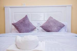 Cama blanca con almohadas moradas y cabecero blanco en Elnara Suites, en Machakos