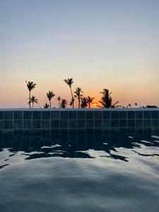a swimming pool with palm trees in the sunset at Pousada Baobá in Jericoacoara