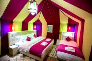 um quarto com 2 camas com paredes cor-de-rosa e roxo em Sahara desert luxurious Camps em Merzouga