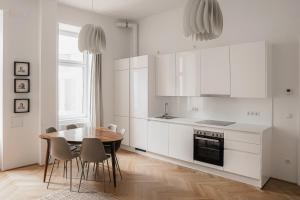 eine Küche mit weißen Schränken sowie einem Tisch und Stühlen in der Unterkunft HeyMi Apartments Zentagasse in Wien