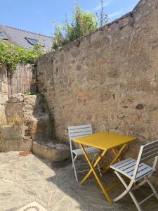 ein gelber Tisch und zwei Stühle neben einer Steinmauer in der Unterkunft La petite maison de Coline in Réville
