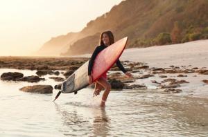 Una mujer caminando en el agua con una tabla de surf en Calipso Ocean Lodge, en Playa Avellana
