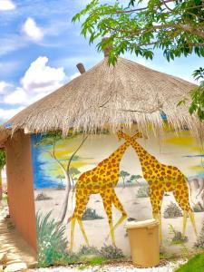 two giraffes standing under a straw hut at Hotel Toolbi in Niaga