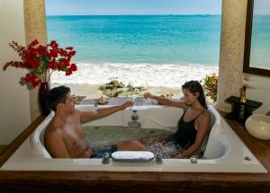 Un uomo e una donna seduti in una vasca da bagno con l'oceano di Hotel Boutique Playa Canela Ecuador a Salinas