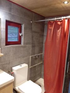 La salle de bains est pourvue de toilettes et d'un rideau de douche rouge. dans l'établissement La p'tite maison bois du hérisson, à Ménétrux-en-Joux