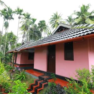 a pink house with palm trees in the background at CAFFEE ISLAND FARM VILLA in Kaniyāmbetta