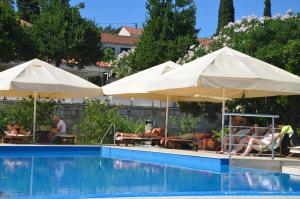 a group of people sitting under umbrellas next to a swimming pool at Hotel Borik in Lumbarda