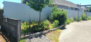 a fence with a garden in front of a house at 8 mins drive to the airport in Christchurch