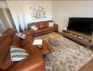 ein Wohnzimmer mit einem Ledersofa und einem Flachbild-TV in der Unterkunft Copper Shores Holiday House in Wallaroo
