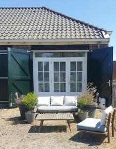 een patio met een bank en een tafel en stoelen bij Kleine studio op boerenerf vlakbij Amsterdam. in Uitgeest