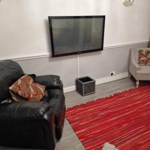 a living room with a black leather couch and a flat screen tv at 5 Bedroom Luxury Home with Garden in East London in Wanstead