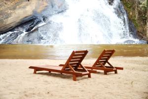 two beach chairs and a bench on the sand near a waterfall at CASA LUXO-água quente-banheira-lareira-cachoeira. in Pedra Azul