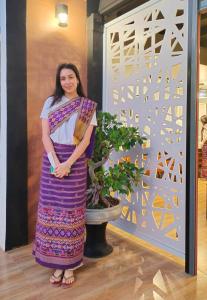 een vrouw in een paarse jurk die naast een plant staat bij โรงแรมเรือนไทย 1 (Thai Guest House) in Ban Don Klang