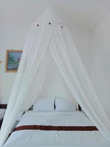 a white canopy bed with white sheets and pillows at Mahakali in Kelimutu