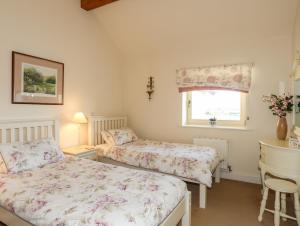 a bedroom with two beds and a desk and a window at Cosy Barn in Dwyran