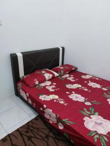 Una cama con un edredón rojo con flores. en Homestay Taman Kota Emas, 