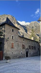 un gran edificio de piedra con montañas en el fondo en CHECK-IN CASAS Casa Benas en Benasque