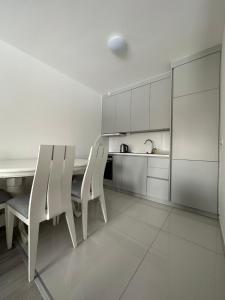 a white kitchen with white chairs and a table at 4-YOU Apartment in Ferizaj