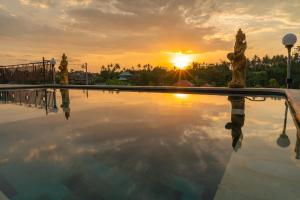 a pool with two statues in front of a sunset at The Pyramid Ubud River Villas in Gianyar