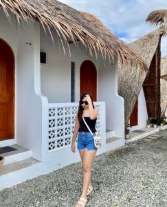 uma mulher em pé em frente a um edifício branco em Hiraya Baler Beachfront Cabanas em Baler