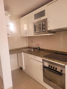 a kitchen with white cabinets and a sink and a microwave at Apartamento funcional en residencial con piscina en inmejorable ubicación en centro de la isla in Caleta De Fuste
