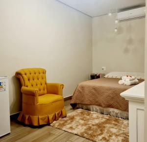 a bedroom with a bed and a yellow chair at Villa Ida Acomodações, 3 suítes aconchegantes e charmosas no centro in Serra Negra
